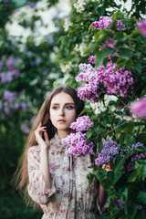 Fototapeta premium Beautiful big-eyed girl near the lilac tree.