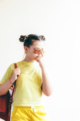 Girl of school age with a sunglasses and school backpack in yellow sportswear. Funny hairstyle. Back to school