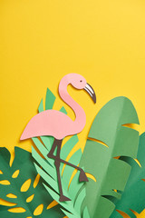 top view of paper cut green palm leaves and cute flamingo on yellow background