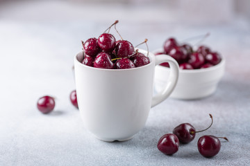 Fresh ripe red cherries in a white mug on a gray stone background Closeup Water drops Top view