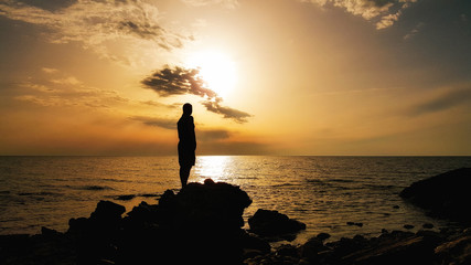Silhouette of a man standing on the rock at the beach on sunset time