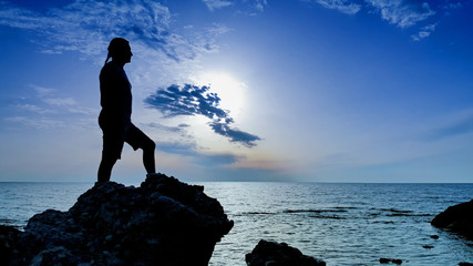 Silhouette of a man standing on large rock at the beach on sunset time