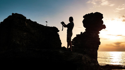 Man silhouette with photo camera in his hands and tripod on the stone.