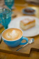 Slice of sweet tasty Honey Cake Medovik and blue cup of cappuccino on the wooden table