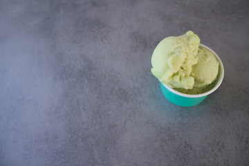 green Apple ice cream sorbet in a turquoise paper Cup on a gray stone table