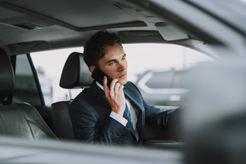 Young handsome guy sitting in his car with smartphone