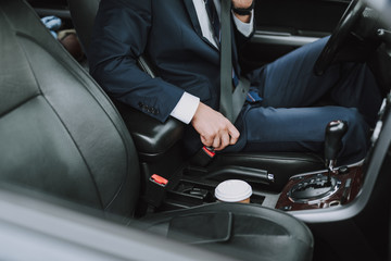 Man in black suit using seat belt in car