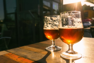 Closeup of two glasses of beer on terrace table with evening sun shining through them. Relaxation, food and drink concept with copy space.