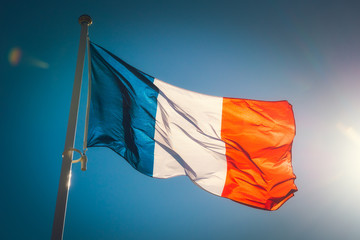 Looking up to a beautiful waving french flag against a blue sky with sunlight.