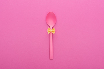 uncooked farfalle pasta on plastic spoon isolated on pink