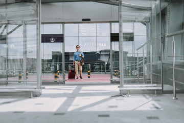 Young male in glasses with bag walking along crosswalk