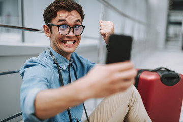 Smiling man holding smartphone and sitting on floor in airport