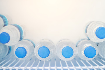 Rows of many transparent plastic bottles with drinking water supply in white refrigerator. Mineral...