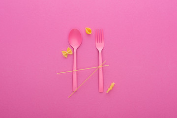 Obraz na płótnie Canvas pink plastic spoon and fork and four different kinds of pasta isolated on pink
