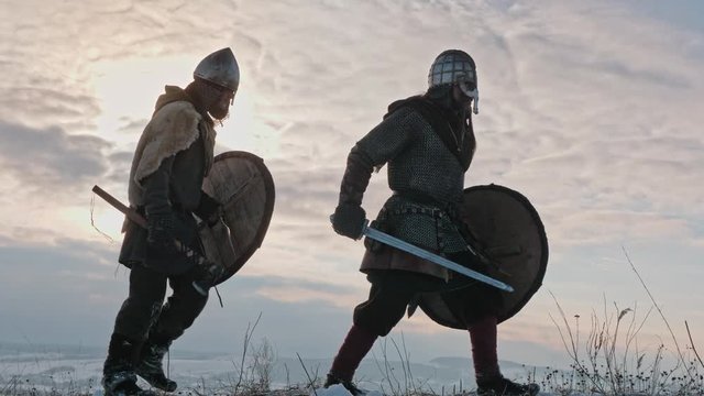 Group of medieval vikings with arms and shields going on the winter meadow.