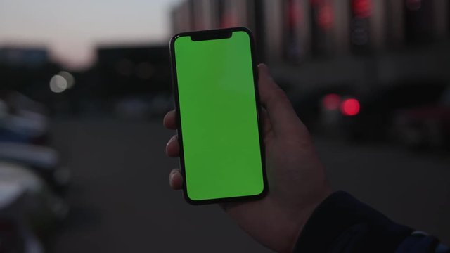 Man hands olding use smartphone with vertical green screen on night city light background car communication device digital gadget phone touchscreen traffic mobile close up