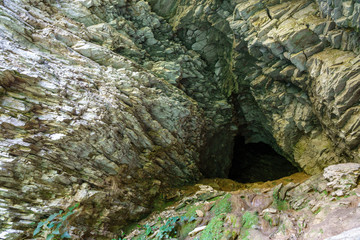 Limestone cliff wall with entrance of the cave. Cave in a layered limestone rock.