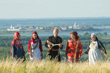 Smiling people in traditional russian clothes walking on the field - a man holding a balalaika