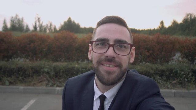 Young happy bearded businessman standing outside office building and taking selfie.
