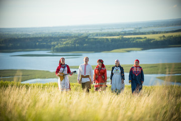 Smiling people in traditional russian clothes walking on the field - a young woman holding a...