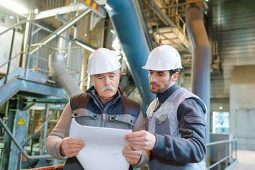 two male workers looking at paperwork in industrial factory