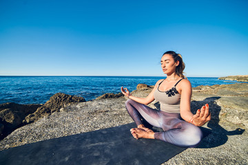 Fototapeta na wymiar Calm young woman meditating at the beach against a beautiful blue sea.
