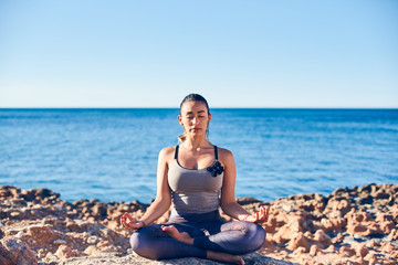 Fototapeta na wymiar Calm young woman meditating at the beach against a beautiful blue sea.