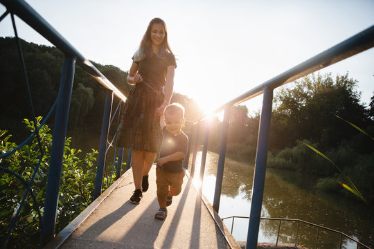 Front view mother and baby son walking on the bridge on lake in summer evening time
