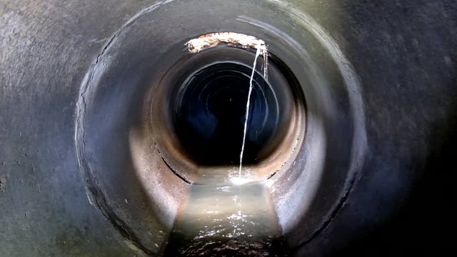 Dark underground sewer round concrete tunnel. Urban sewage flowing throw sewer pipe