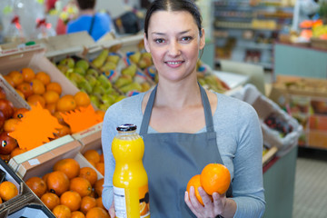 portrait of female grocer holding oranges and bottle of juice
