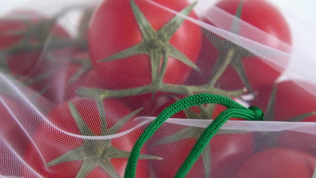 A ripe branch of cherry tomato lies in a reusable reuse bag on an isolated white background. to deal with disposable plastic bags close up mesh texture