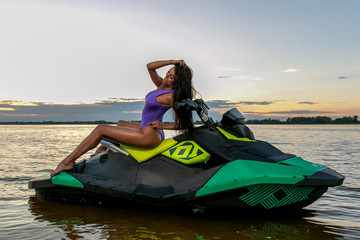 Young sexy girl in a blue swimsuit posing, sitting on a jet ski on the river in a sunshine. Summer weekend or vacation. Extreme sport