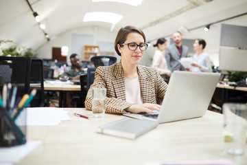 Obraz premium Portrait of contemporary businesswoman using laptop while working in open space office