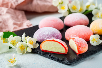 Multi-colored Japanese ice cream Mochi in rice dough and Jasmine flowers on a concrete blue background. Traditional Japanese dessert on a black slate