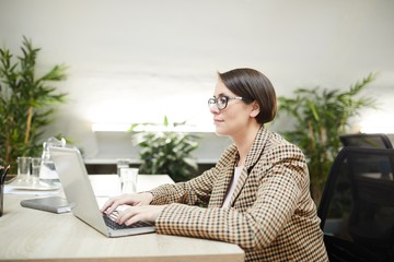 Side view portrait of contemporary businesswoman using laptop while working in office