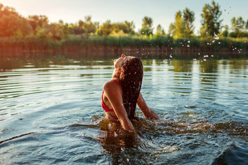 Young woman in bikini jumping out of water and making splash. Summer vacation