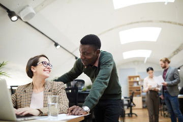 Portrait of young African businessman smiling at female colleague while working in office, copy space