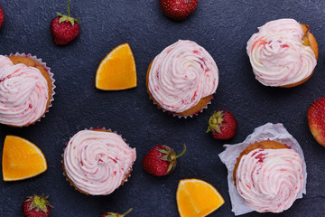 Orange cupcake with strawberry filling and butter cream with fresh berries. Dessert on a dark wooden board. Top view.