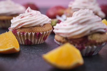 Orange cupcakes with strawberry filling and butter cream with fresh berries. Desserts on a dark background.