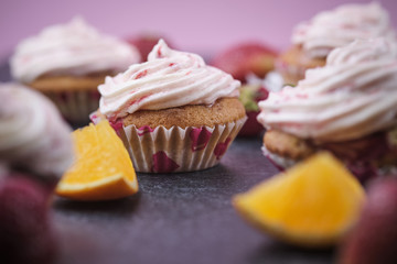 Orange cupcakes with strawberry filling and butter cream with fresh berries. Desserts on a dark background.