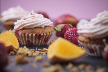 Orange cupcakes with strawberry filling and butter cream with fresh berries. Desserts on a dark background.