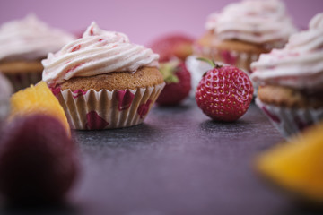 Orange cupcakes with strawberry filling and butter cream with fresh berries. Desserts on a dark background.