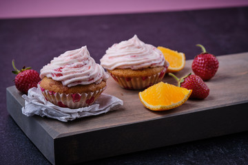 Orange cupcake with strawberry filling and butter cream with fresh berries. Dessert on a dark wooden board.