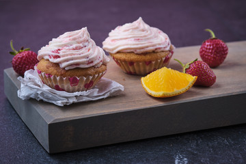 Orange cupcake with strawberry filling and butter cream with fresh berries. Dessert on a dark wooden board.