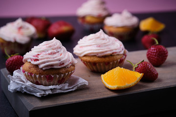 Orange cupcake with strawberry filling and butter cream with fresh berries. Dessert on a dark wooden board.