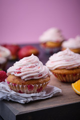 Orange cupcake with strawberry filling and butter cream with fresh berries. Dessert on a dark wooden board.
