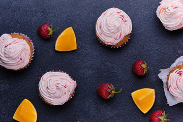 Orange cupcake with strawberry filling and butter cream with fresh berries. Dessert on a dark wooden board. Top view.