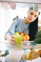 Smiling woman taking a fresh fruit out of the fridge, healthy food concept