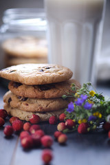 American chocolate cookies. Cookies in a can. A stack of cookies in the shape of a tower. Cookies, a glass of milk, strawberries, flowers and a linen towel. Rural still life.