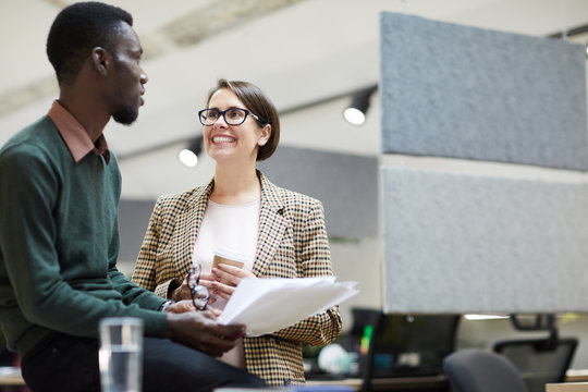 Portrait of young business manager smiling cheerfully at African-American colleague while chatting at break in office, copy space
